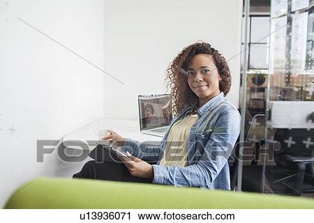 Stock Image - Portrait of young woman using digital tablet at office desk. Fotosearch