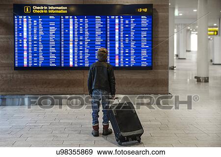 Rear view of boy with wheeled suitcase looking at airport departure board View Large Photo Image Stock Photo - Rear view of boy with wheeled suitcase looking at airport departure board. Fotosearch