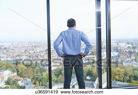 Stock Photo - "Rear view of businessman looking from office window at Brussels cityscape, Belgium". Fotosearch