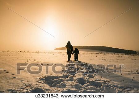 Stock Image - "Rear view of man and son walking in snow covered landscape at sunset, Sarsy village, Sverdlovsk Oblast, Russia". Fotosearch