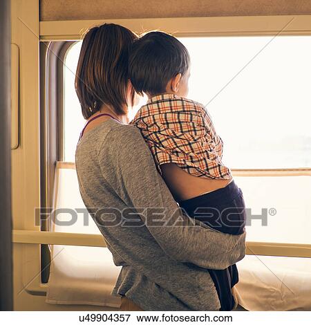 Rear view of woman and toddler son looking out of sunlit train window View Large Photo Image Stock Photo - Rear view of woman and toddler son looking out of sunlit train window. Fotosearch