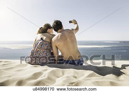 "Rear view of young couple taking selfie, Dune de Pilat, France" View Large Photo Image Stock Image - "Rear view of young couple taking selfie, Dune de Pilat, France". Fotosearch
