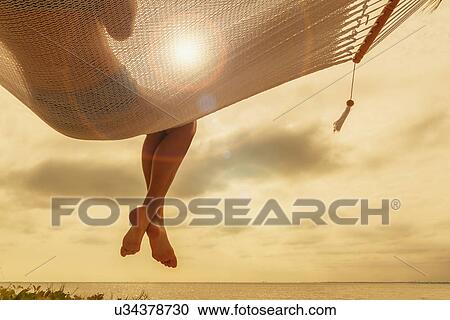 Stock Image - "Rear view of young woman reclining on hammock at dusk on Miami Beach, Florida, USA". Fotosearch