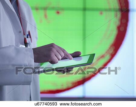 Stock Image - "Scientist using digital tablet in front of graphical display of silicon wafer on screens, close up". Fotosearch