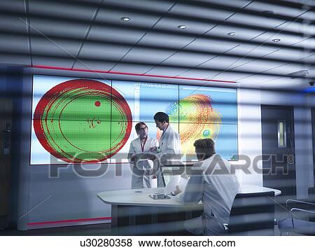 Stock Photo - Scientists in meeting in front of graphical display of silicon wafer on screens. Fotosearch