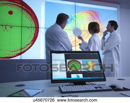 Stock Photograph - Scientists in meeting in front of graphical display of silicon wafer on screens. Fotosearch