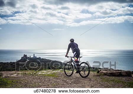 Stock Photo - "Silhouetted view of male mountain biker on coastal path, Cagliari, Sardinia, Italy". Fotosearch