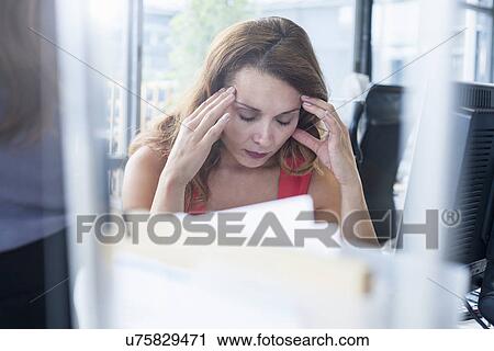 Stock Image - Stressed businesswoman at office desk. Fotosearch