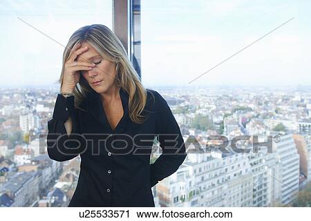 Stock Image - "Stressed businesswoman in front of office window with Brussels cityscape, Belgium". Fotosearch