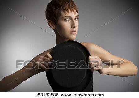 Stock Photograph - Studio portrait of woman holding top hat in front of chest. Fotosearch