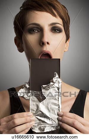 Studio portrait of woman holding up dark chocolate bar to mouth View Large Photo Image Stock Image - Studio portrait of woman holding up dark chocolate bar to mouth. Fotosearch