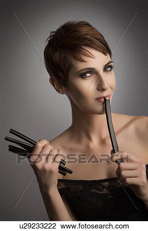 Stock Image - Studio portrait of woman holding up licorice stick to her lips. Fotosearch