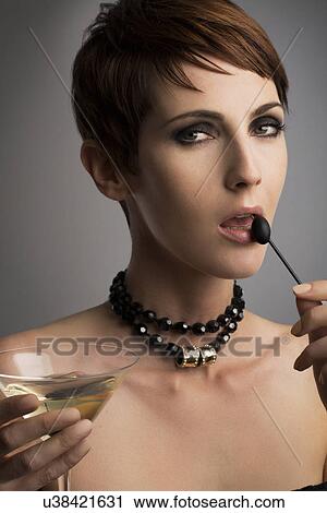 Stock Image - Studio portrait of woman looking sideways holding black olive cocktail stick to her lips. Fotosearch