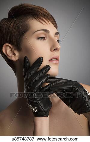 Stock Photo - Studio portrait of woman with hand on her cheek wearing black leather gloves. Fotosearch