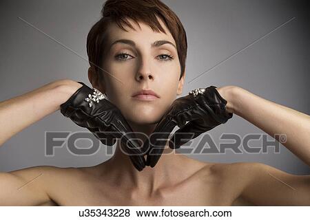 Stock Photo - Studio portrait of woman with hands on chin wearing black leather gloves. Fotosearch