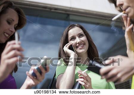 Picture - Three businesswoman using mobile phones and smoking outside office. Fotosearch