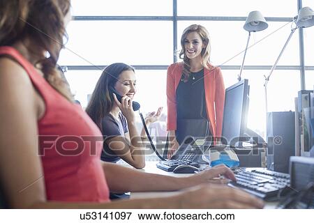 Stock Photo - Three businesswomen chatting at office desk. Fotosearch