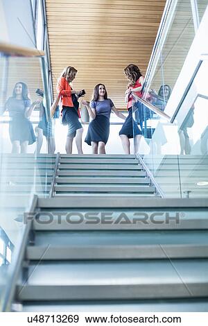 Stock Photo - Three businesswomen chatting at top of office stairs. Fotosearch