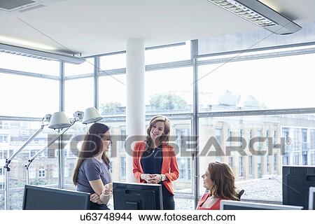 Picture - Three businesswomen discussing ideas at office desk. Fotosearch