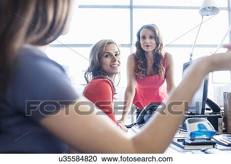 Three businesswomen having informal meeting at office desk View Large Photo Image Stock Image - Three businesswomen having informal meeting at office desk. Fotosearch