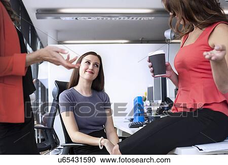 Stock Image - Three businesswomen having informal meeting at office desk. Fotosearch