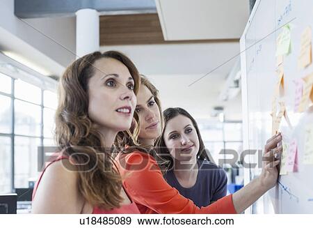 Stock Photo - Three businesswomen presenting ideas on office whiteboard. Fotosearch