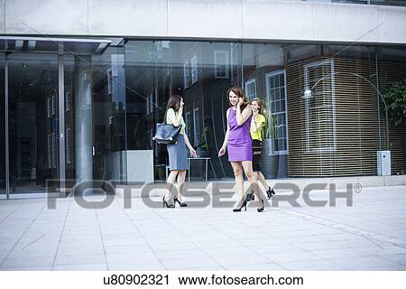 Stock Image - Three businesswomen using mobile phones and smoking outside office. Fotosearch