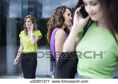 Stock Photo - Three businesswomen using mobile phones outside office. Fotosearch