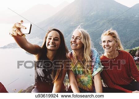 Picture - "Three female friends taking smartphone selfie at Lake Atitlan, Guatemala". Fotosearch