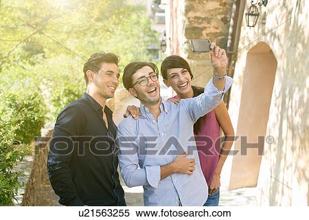 Stock Photography - Three young adult friends taking smartphone selfie in park. Fotosearch