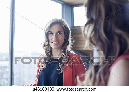 Stock Photo - Two businesswomen having informal meeting in front of office window. Fotosearch