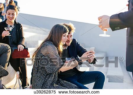 Stock Photography - "Two friends taking self portrait at party, using smartphone". Fotosearch