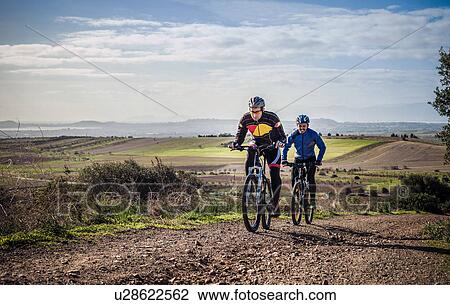 "Two male mountain bikers cycling up dirt track, Cagliari, Sardinia, Italy" View Large Photo Image Stock Image - "Two male mountain bikers cycling up dirt track, Cagliari, Sardinia, Italy". Fotosearch