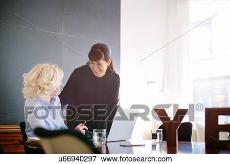 Stock Photo - Two mature businesswomen chatting at boardroom table. Fotosearch