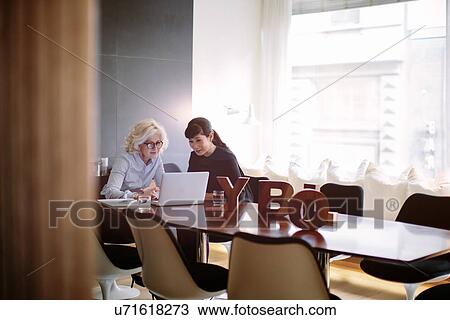 Stock Image - Two mature businesswomen using laptop at boardroom table. Fotosearch