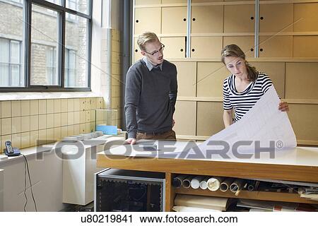 Two young designers looking at blueprint in creative office View Large Photo Image Stock Image - Two young designers looking at blueprint in creative office. Fotosearch