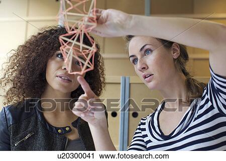 Two young female designers looking at handmade model in creative office View Large Photo Image Stock Image - Two young female designers looking at handmade model in creative office. Fotosearch