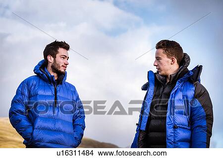 Picture - "Two young male hiking friends chatting, The Lake District, Cumbria, UK". Fotosearch