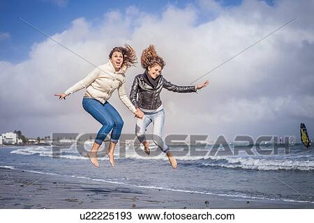Two young women friends holding hands and jumping on beach View Large Photo Image Stock Image - Two young women friends holding hands and jumping on beach. Fotosearch