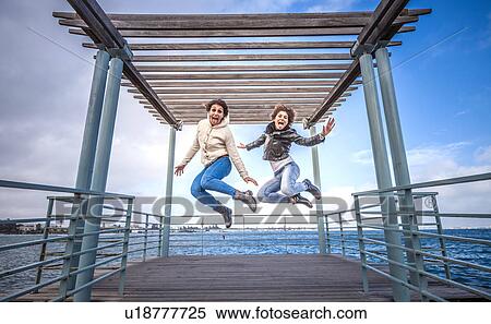 Two young women friends jumping in unison on sea pier View Large Photo Image Stock Photography - Two young women friends jumping in unison on sea pier. Fotosearch