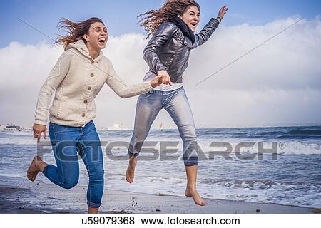 Stock Photo - Two young women friends running and jumping on beach. Fotosearch