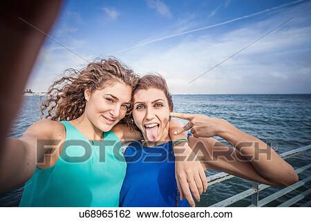 Stock Image - Two young women friends taking selfie on pier. Fotosearch