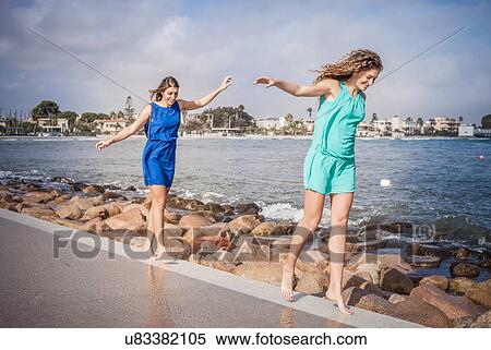 Stock Photography - Two young women friends walking barefoot along promenade. Fotosearch