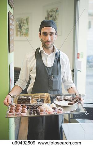 Stock Photo - Waiter carrying tray of cakes and cookies in cafe. Fotosearch