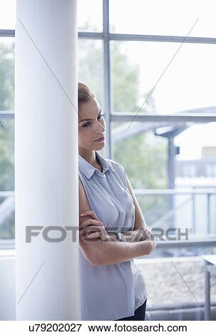 Stock Photo - "Woman crossing arms, leaning against pillar". Fotosearch