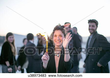 Stock Image - Woman holding mini firework at outdoor party. Fotosearch
