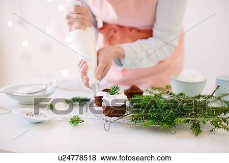 Stock Photo - Woman icing chocolate cupcakes with whipped cream. Fotosearch