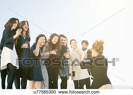 Stock Image - Woman taking photograph of group of friends at party. Fotosearch