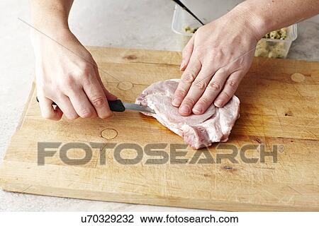 Stock Image - Womans hands slicing pork steaks on chopping board. Fotosearch