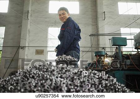 Picture - "Worker shovelling metal components used in crane manufacturing facility, China". Fotosearch